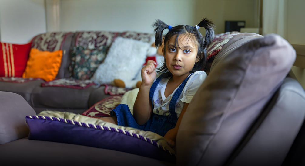 Young girl with pigtails sitting on a couch in her living room staring at the camera.