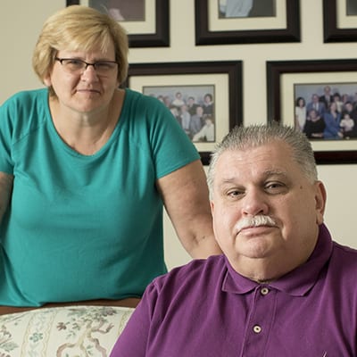 Middle aged husband and wife smiling while sitting on their living room couch.